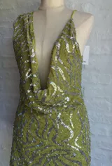 Vestido corto ajustado color verde lima, con escote pronunciado en V tipo drapeado y tirantes finos. El vestido está cubierto de lentejuelas plateadas.