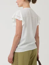 Blusa blanca de lino orgánico y viscosa, con cuello redondo, cierre frontal con botones, mangas cortas con volados y broderie con calados en el frente.