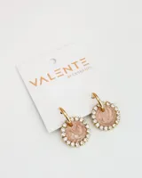 Aros colgantes dorados con forma circular. El círculo está decorado con strass y tiene un centro con diseño marmolado en tonos rosados y blancos.