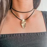 Collar con diseño de hoja en metal dorado, con cordón de cuero negro en doble cinta.