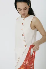 Top sin mangas de lino color crudo, con cartera asimétrica y botones de madera. Tiene ojales bordados con forma de frutillas.