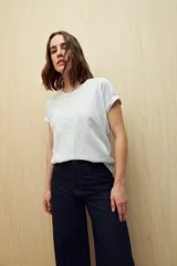 Remera de manga corta color gris claro, confeccionada en algodón con textura liviana y suave al tacto. Presenta costuras decorativas en los laterales y mangas con pequeño doblez.