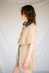 Vestido corto verde militar de microfibra con cuello camisero negro, cintura elastizada con cordón de ajuste y mangas cortas con dobladillo. Cierre frontal con botones.