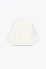 Blazer blanca de cuello solapa y manga corta con vuelta. Bolsillos delanteros de vivo y cierre frontal cruzado con botones.
