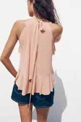 Top color rosa viejo de cuello halter ajustable con lazadas. Detalle de abertura en el delantero y volantes en el mismo tejido.