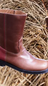 Botas de media caña color marrón de cuero vacuno, con detalle de costuras en la capellada y contrafuerte color bordó. Suela de caucho con taco bajo.