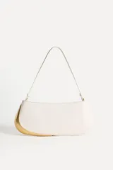 Bolso de hombro alargado color crema, con asa corta y detalle metálico dorado en un lateral. Tiene un bolsillo interior con cremallera y cierre principal con cremallera.
