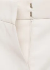 Pantalón de vestir color crema, de corte recto, con cierre de botón y cremallera, tiro medio y bolsillos laterales.