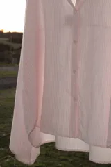 Camisa oversize color rosa claro a rayas verticales blancas, con cuello mao y mangas largas con puños elásticos.