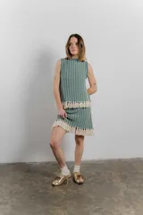 Conjunto tejido de poliéster y algodón, compuesto por un top sin mangas y una minifalda a rayas con flecos. Ideal para el verano, con un estilo boho y relajado.