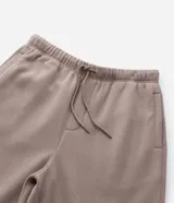 Pantalón baggy color beige, confeccionado en algodón con felpa. Presenta cintura elástica con cordón ajustable, bolsillos delanteros y un bolsillo trasero. El bajo es ajustable con elástico.