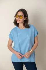 Blusa italiana color celeste con bordado de plumas al tono en el frente, confeccionada en lino y algodón.