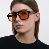 Lentes de sol aviador oversize con montura geométrica negra y lentes color naranja. Cuentan con doble puente, montura fina y bordes biselados. Protección UV400.