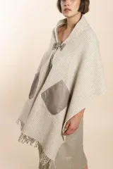 Chal de lana fina sin teñir, con calce en hombros, abrochadura con alamar de fieltro, bolsillos de cuero y terminación con flecos. Diseño exclusivo de Don Baez, hecho en Uruguay.