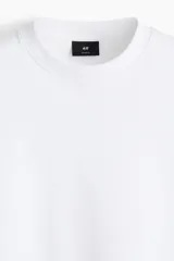 Remera blanca de algodón pesado, corte boxy holgado, cuello redondo ribeteado y hombros caídos.