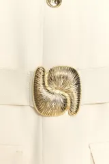 Vestido midi color crema, de cuello redondo y sin mangas. Presenta falsos botones frontales, cinturón elástico con aplique dorado, bolsillos de parche con solapa y abertura delantera.