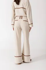 Pantalón de vestir color manteca, de corte recto y tiro alto, con detalle de ribetes marrones en los laterales.