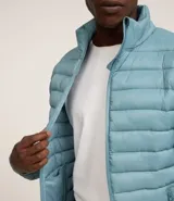 Campera puffer ultraligera color beige, con cuello alto, cierre por cremallera y bolsillos con cremallera. Incluye bolso de almacenamiento.