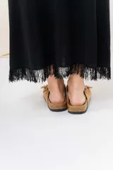 Vestido midi color beige, de tejido tipo seda, con escote redondo, sin mangas y detalle de flecos en el ruedo.