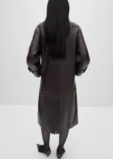 Abrigo largo oversize de cuero ovino color marrón oscuro, con cuello camisero, cierre frontal oculto con cremallera, mangas largas con puños abotonados, forro interior y dos bolsillos laterales.