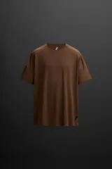 Remera deportiva marrón de tejido técnico, ligero y elástico con estructura perforada. Cuello redondo, manga corta, bajo asimétrico con aberturas laterales, costuras termofijadas y logo estampado.