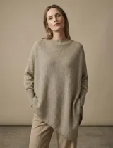 Poncho de tejido lurex color verde oliva con brillo sutil, de corte amplio y manga larga con puños acanalados. Presenta un bajo asimétrico con caída diagonal.