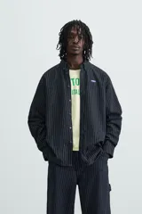 Camisa negra con finas rayas verticales blancas, de corte holgado, manga larga y cuello abotonado.