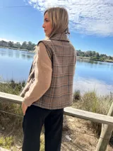 Chaleco marrón a cuadros con botones dorados y bolsillos delanteros.