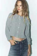 Camisa de manga larga con puños elásticos y cuello bobo con volantes. Cierre frontal con botones.