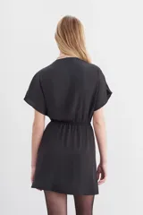 Vestido mini negro con escote cruzado, mangas cortas y cintura elastizada con lazo. Presenta cadenas metálicas en los hombros y en la terminación del lazo.