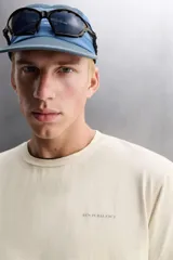 Camiseta color crema de corte holgado, cuello redondo y manga corta. Presenta un pequeño estampado con texto en el lado izquierdo del pecho.