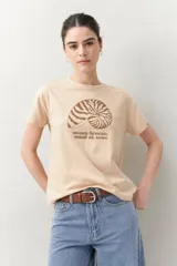 Remera blanca de manga corta con estampado de una concha marina y la frase "ocean breeze, mind at ease" en color marrón.