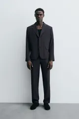 Pantalón de vestir negro de corte relaxed fit confeccionado en tejido con lana. Cuenta con bolsillos frontales y traseros de doble vivo con botón. Cierre frontal con cremallera y botón.