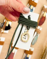 Gargantilla choker con tiento de gamuza verde oscuro y dije circular calado color crema con aplique dorado.