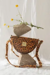 Bandolera de cuero con estampado animal print de leopardo, forma de media luna y correa ajustable.