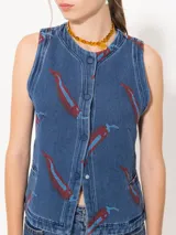 Chaleco denim azul con estampado de pimientos rojos, cuello redondo, pinzas de entalle, bolsillos sastreros y cierre frontal con broches.