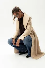 Trench largo de cuero color beige con forro azul, cuello clásico, cierre frontal con botones y bordado de las "S" en el frente.