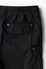 Short cargo negro de popelina de algodón, con cintura elástica ajustable con cordón, bolsillos laterales, bolsillos cargo con solapa y botón a presión en piernas y traseros, y aberturas laterales en el bajo.