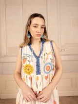 Vestido largo color crema con estampado de flores y corazones en tonos azules, naranjas y amarillos. Tiene cuello en V con ribete azul y corte imperio con falda escalonada.