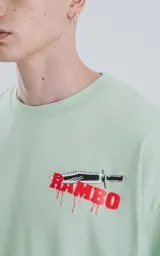 Remera verde agua de manga larga con corte oversize y hombros caídos. Estampado frontal con el nombre "Rambo" en rojo y negro, con una daga cruzada.