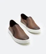 Championes slip on marrones de cuero, con talón flexible y suela blanca.