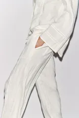 Pantalón blanco de lino con tiro medio, cintura ajustable con cordones, bolsillos laterales ocultos y detalle de entredós combinados a tono.