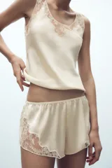 Shorts tipo lencero color crema confeccionado en tejido satinado con tiro alto, cintura elástica y detalle de encaje a tono en el ruedo.