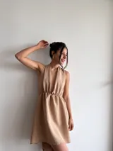 Vestido corto color beige, con escote halter y espalda descubierta. Presenta cintura elastizada y falda con vuelo.