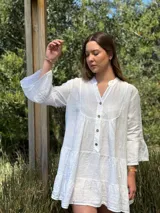 Vestido corto blanco de lino, con cuello mao, botones de coco y mangas 3/4 acampanadas. Diseño amplio con volados en ruedo y mangas.