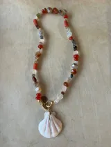 Collar largo de cuentas de piedras semipreciosas en tonos tierra, con dijes de conchas marinas.