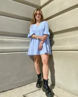 Vestido corto celeste y blanco con estampado de cuadrillé, escote en V, mangas 3/4 con volados y botones decorativos.