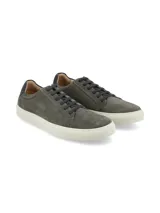 Zapatilla urbana de hombre, estilo casual, color gris oscuro o topo, confeccionada en gamuza. Presenta cordones oscuros y suela de goma blanca gruesa. El talón tiene un detalle de refuerzo en material liso de color verde oscuro o azul marino.