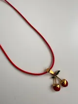 Gargantilla con cordón rojo y dije de cerezas rojas con detalles dorados y hojas verdes.