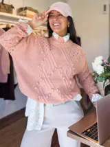Sweater tejido grueso color rosa, con cuello alto, mangas largas y diseño trenzado con detalles de pompones.